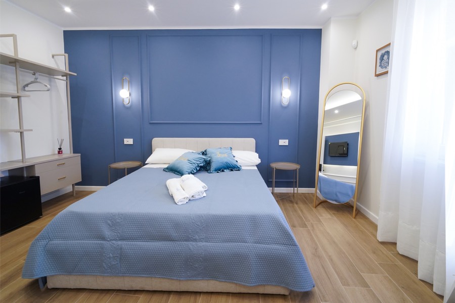 Camera Iris: parete blu con libreria a giorno, minibar e scrivania