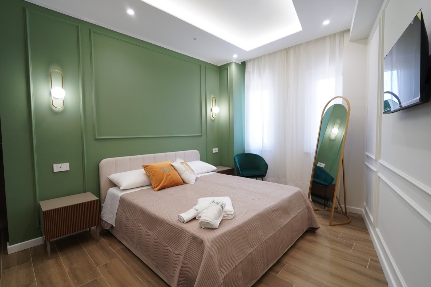 Camera Verde: letto matrimoniale, parete in boiserie verde salvia, poltrona in velluto e specchio ad arco dorato